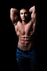 Fototapeta na wymiar Attraktiver muskulöser junger Mann posiert mit angespannten Muskeln, Portrait vor schwarzem Hintergrund mit copy space 