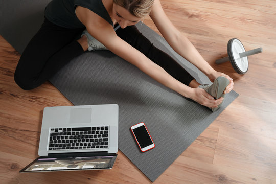 Young caucasian woman doing online workout and repeating exercises from online training on laptop. Flexibility and strength.Wellness and home fitness concept