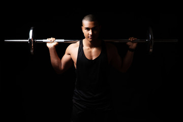 Fototapeta na wymiar Attraktiver und muskulöser Mann posiert mit Hanteln vor schwarzem Hintergrund 
