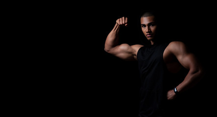 Attraktiver muskulöser junger Mann posiert mit angespannten Muskeln, Portrait vor schwarzem Hintergrund mit copy space  - obrazy, fototapety, plakaty