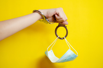 female hand wearing handcuffs and mask on yellow background