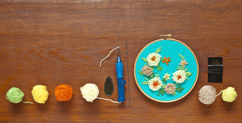 Needlework and embroidery. A special needle using the technique of punching tapestry and wool balls on a wooden background. Delicate floral ornament embroidered on green canvas. Flat lay, copy space