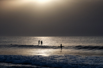 Surfer and sup surfers silhouette in the water at sunset with sea background