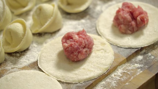 Meat ball on a piece of dough, cooking dumplings, close-up. Rows of prepared dumplings lie on a wooden board. Making of meat dumpling at home. Close up male hands makes dumplings with minced meat.