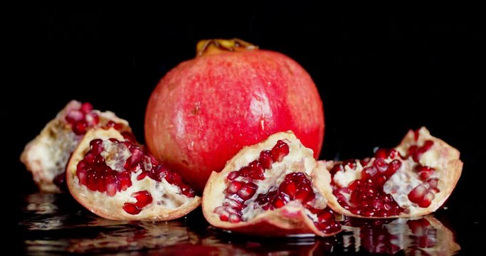 On whole and slices ripe pomegranate falling water drops.