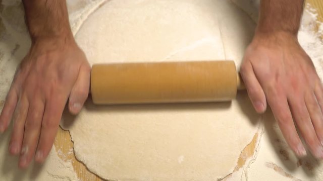 Man rolls dough with rolling pin for pita breads. Baker, Chef hands preparing fresh dough with rolling pin on kitchen table at cuisine of restaurant or bakery. Professional cooking and food concept