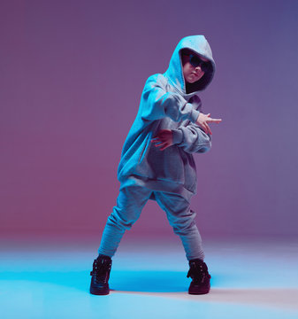 Cool boy child dancing hip hop in a hoodie and glasses, in a Studio on a neon background.