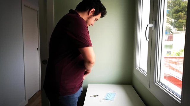 Young Caucasian Man Getting Ready To Leave His Home, Picking His Wallet, The Keys And Putting A Medical Mask On