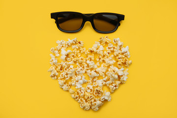 Love Cinema concept of popcorn arranged in a heart shape and glasses on yellow background.