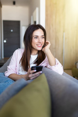 Young woman sitting on sofa in living room at home, doing online shopping through 3G internet, having smart phone in hands