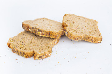 Three sliced pieces of brown bread with cereals. Crumbs laying around. Traditional rye loaf slices isolated on white background. Studio shot. Side view. Homemade bakery and nutrition concept