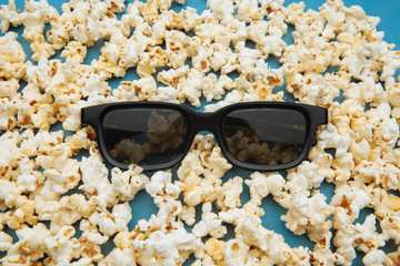 Popcorn and 3d glasses for the movie are on blue backgound. Top view.