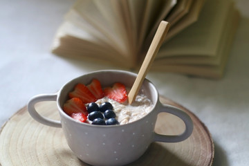 Bowl of porridge with fruit and open book on a bed. Selective focus.