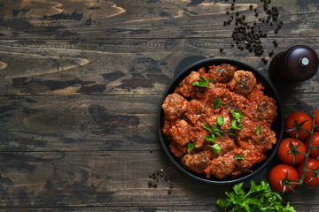 Frying pan with meat balls with tomato sauce on a wooden background.