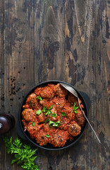Frying pan with meat balls with tomato sauce on a wooden background.
