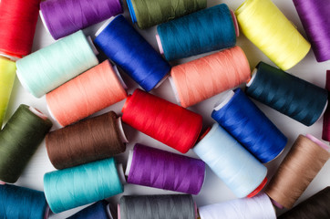 Top view of colorful bobbins on the white surface.Different colors of spools of thread