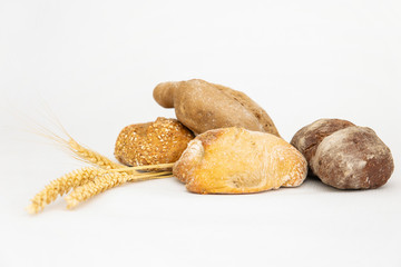 Many different delicious breads and three ears of wheat. Crispy loafs and buns made of wheat and rye flour isolated on white background. Studio shot. Side view. Homemade bakery and nutrition concept