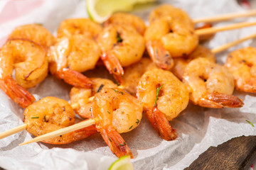 close up view of prawns on skewers with lime on parchment paper on wooden board