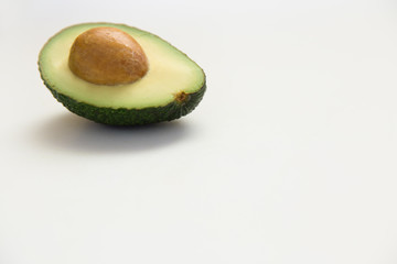 Single cut half of avocado fruit with core. Closeup, copy space. Isolated object on white background. Fresh food or advertising