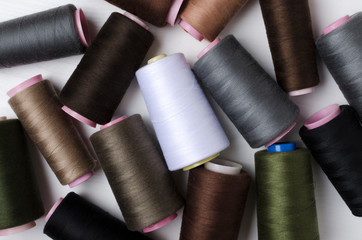Top view of spools of dark colors threads on the white surface