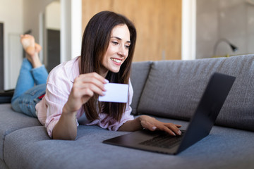 Young woman entering her credit card numbers on a website while lying on a sofa. Shopping online.