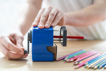 close-up of women's hands using a blue pencil sharpener at the table, school concept
