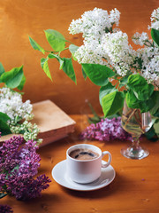 Romantic background of Breakfast . A Cup of fragrant espresso coffee on a wooden table with a bouquet of white and purple lilacs and a book