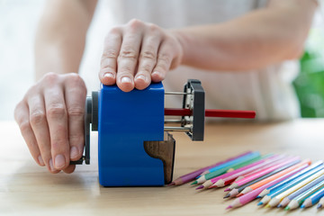 Obraz premium close-up of women's hands using a blue pencil sharpener at the table, school concept
