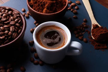Fotobehang Fresh espresso cup, roasted and ground beans in clay bowls, wooden spoon on dark blue table surface. Closeup, high angle. Coffee shop, morning, baristas workplace  concept © Евгения Савина