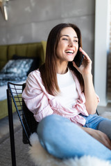 Beautiful woman talking by mobile phone while sitting in armchair at home