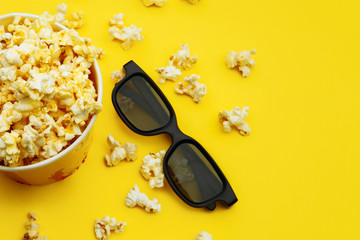 Popcorn in a bowl and 3d glasses on yellow background, top view.