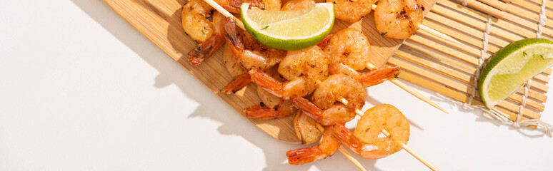 top view of prawns on skewers with lime on bamboo mat on white background, panoramic orientation