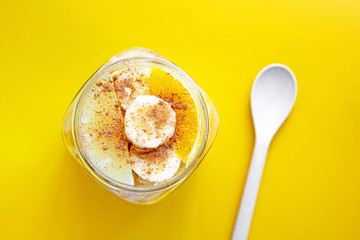 Sliced fruit sprinkled with cinnamon in a jar and a spoon made of biodegradable plastic consisting of natural fibers of wheat, starch and food grade polypropylene. Yellow background. Eco concept