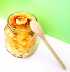 Sliced fruit sprinkled with cinnamon in a jar and a spoon made of biodegradable plastic consisting of natural fibers of wheat, starch and food grade polypropylene. Green wall background. Eco concept