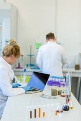 Obraz na płótnie Canvas Chemist with rubber gloves working on laptop in laboratory