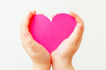 Closeup of paper heart in little hands of child on white background. Pink heart in hands on white.
