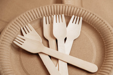 Wooden forks and plates on kraft paper background. Eco friendly disposable tableware. Also used in fast food, restaurants, takeaways, picnics. Top view. Copy, empty space for text