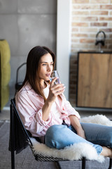Young girl drinking water sitting on a couch at home and looking at camera