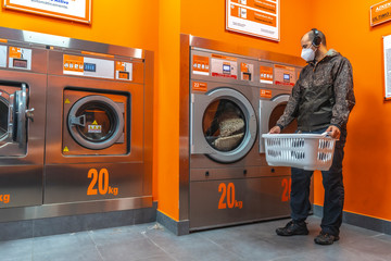 A young man with a mask for the covid-19 waiting in the laundry. Social distance, coronavirus...