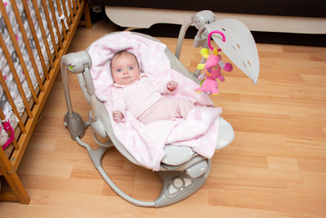 Cute little two month old baby girl lying in the baby rocking chair and watching the hanging toy