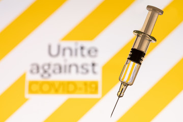 Text Unite against COVID-19 with glass syringe on yellow background. Concept about vaccine of coronavirus or COVID-19.