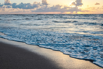 Sunset at the rocky sea. Turquoise water in the ocean in the evening.Yellow sky with small clouds and blue waves at sandy beach at the seaside.Paradise resort landscape.Close-up picture of ocean waves
