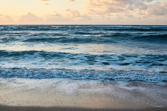 Sunset at the rocky sea. Turquoise water in the ocean in the evening.Yellow sky with small clouds and blue waves at sandy beach at the seaside.Paradise resort landscape.Close-up picture of ocean waves