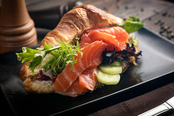 French croissant with salmon, salad, cucumber, sauce on dark plate 