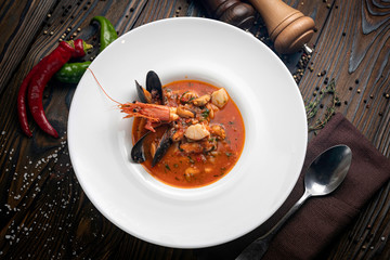 Thai tom yam soup with seafood in a white plate on a wooden background

