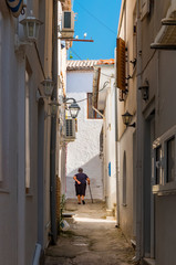 An old greek woman is walking the street of Parga, between white houses.