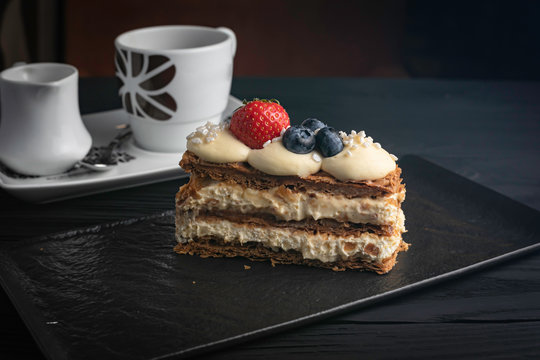 French dessert Milfey cake, with berries on a black plate and a dark background