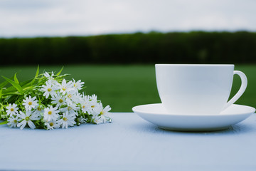 Cup of coffee and wildflowers on the table overlooking the green field. In the open. The concept of breakfast
