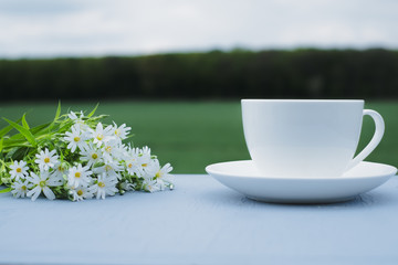 Cup of coffee and wildflowers on the table overlooking the green field. In the open. The concept of breakfast
