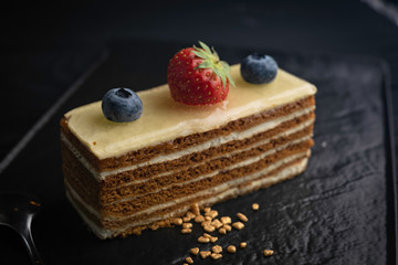 honey cake with berries on a dark dish and a black background. 